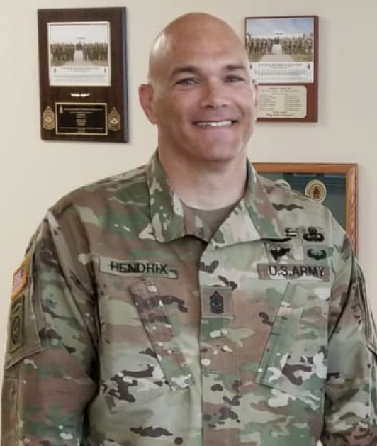 A man in military fatigues standing next to two plaques.